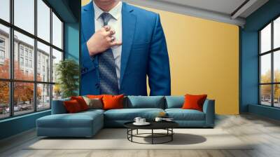 Business man straightens his tie. Yellow background. Wall mural