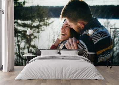 Joyful cute couple embraces. Young man in a sweater hugs a girl from behind background in winter. The concept of a successful relationship and happy moments Wall mural