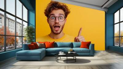 Excited energetic young man with glasses and curly hair making an enthusiastic gesture and facial expression against a bright yellow studio background  Concept of positive lively Wall mural