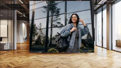 Happy young woman walking on city streets with a leather backpack, smiling. Wall mural