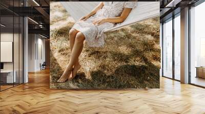 Legs of a barefoot woman sitting on hammock in the garden. Wall mural