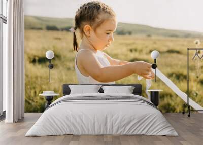 Little girl in an open field on a summer playing with a white ribbon. Wall mural