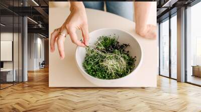 Woman taking organic green sprouts from a bowl. Wall mural