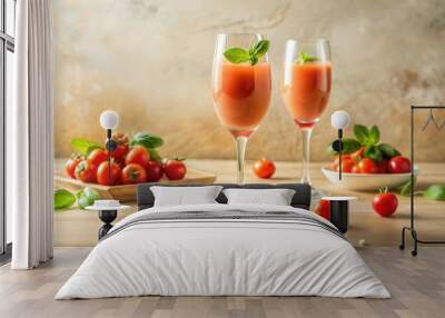 An editorial style photo of the pink-colored sweet and sour tomato cocktail in a champagne glass, with two fresh tomatoes on one side and basil leaves on top. The light beige background has soft shado Wall mural