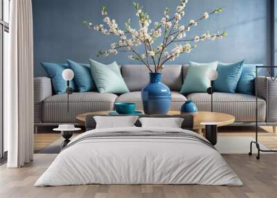 minimalist Art deco, shabby chic interior design of modern living room, home. Close up of blue ceramic vase with blossom branch on round wooden coffee table against sofa with blue pillows Wall mural