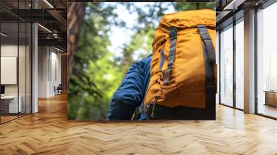 A person is wearing a yellow backpack and is standing in front of a large tree. The backpack is on their back and is visible from the front. Concept of adventure and exploration Wall mural