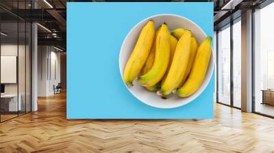 Banana fruit in white bowl on blue background. Wall mural