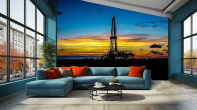 A drilling rig silhouetted against the dawn sky, with the first light of day breaking over the horizon. The rig stands tall Wall mural