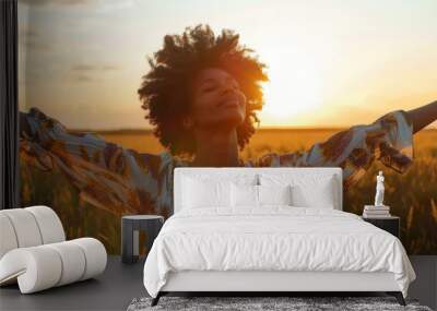 A beautiful peaceful afro-haired woman with closed eyes stretches her arms enjoying the fresh air in a field at sunset Wall mural