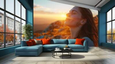 A beautiful peaceful woman in her thirties with her eyes closed and arms outstretched, breathing fresh air on a mountain hill at sunrise Wall mural