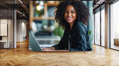 Photo of beautiful young professional African-American woman with curly hair, smiling, using laptop in bright and stylish office space Wall mural