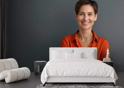 Portrait of a happy businesswoman wearing a business casual orange shirt with crossed arms and smiling at the camera on a gray background Wall mural