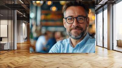 Satisfied male businessman in modern semi-formal wear and glasses smiling happily on blurred cafe indoor background Wall mural