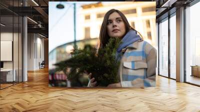 Horizontal photo. Soft focus. Cute young adult child free white brunette woman on street fair with fir branches. Christmas market with decorations. Winter holiday, gift. Sun day. Happy New Year 2025.  Wall mural