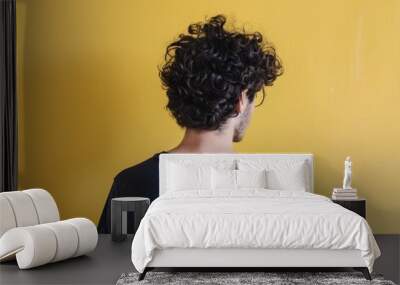 Young man with curly hair stands against a bright yellow wall Wall mural