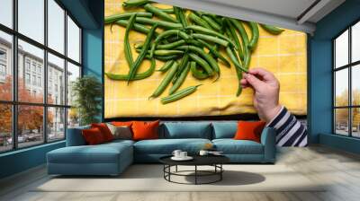 Child hand is taking ripe raw tasty healthy green beans from the rustic wooden table, close up shot Wall mural