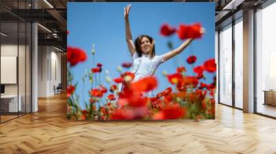 Happy girl in blue dress dancing in field of red poppies with hands in the air. Country life. Sunny day. Wall mural