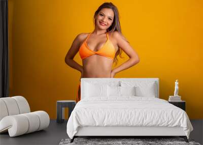 Attractive girl in a orange bikini, hat, emotionally opened mouth on a bright yellow background with a perfect body. Isolated. Studio shot. Wall mural