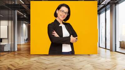 Attractive middle aged woman with beautiful smile on yellow wall. Pretty older business woman, successful confidence with arms crossed. Wall mural