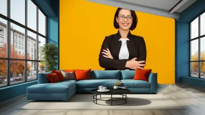 Attractive middle aged woman with beautiful smile on yellow wall. Pretty older business woman, successful confidence with arms crossed. Wall mural