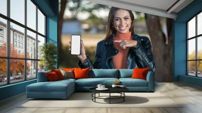 beautiful smiling latin american woman pointing to the left at cellphone with blank screen Wall mural