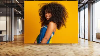 Happy black woman fan holding a Brazilian flag. Brazil colors in background, green, blue and yellow. Elections, soccer or politics. Wall mural