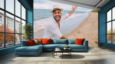 Smiling latin american man on the beach gesturing to the space on the right with his palm Wall mural