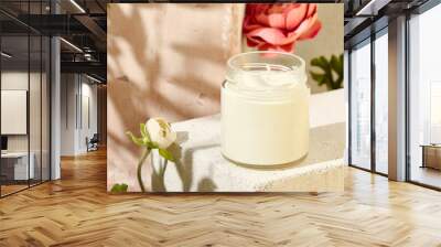 Composition with aromatic candle in jar on concrete podium. Mockup soy wax candle in natural style with flower. Scented handmade candle with wick.  Handmade spa product  from soy wax in glass. Wall mural