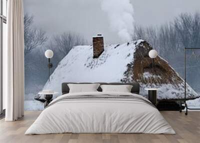 A small cottage with smoke billowing from the chimney in the winter snow. Covered with a blanket of frosty snow cover Wall mural