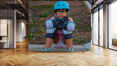 Vertical shot of a kid sitting wearing roller skates, a helmet, and knee pads Wall mural