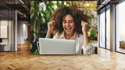 Excited biracial woman cheers while using laptop after winning an online prize or contest Wall mural