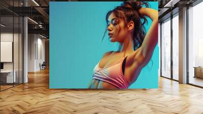 Fit young woman wearing tank top and shorts, posing on solid blue background Wall mural