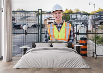 Happy young construction worker wearing safety gear and holding a clipboard. Wall mural