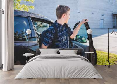 Teenager closing the door of his car that is parked in a school parking lot. Wall mural