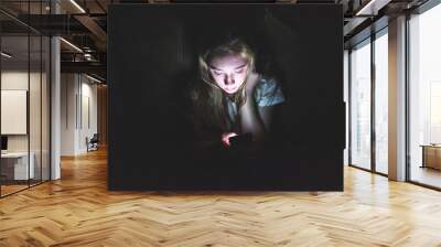 upset girl sitting in the dark while using her smartphone. the light from the screen is illuminating Wall mural