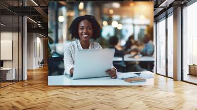 A woman is sitting at a desk with a laptop open in front of her. She is smiling and she is happy. The scene suggests a positive and productive work environment,banner Wall mural