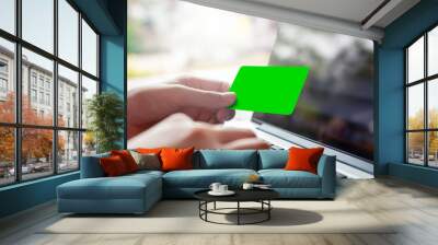 hand holding blank green credit card and using modern laptop, typing and texting. against defocus green nature outdoor.  mobile payment ,online shopping concept Wall mural