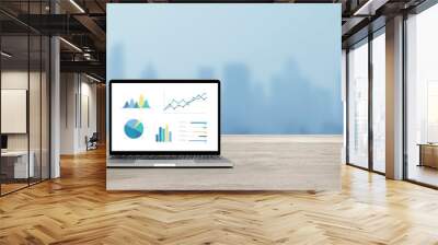 Modern laptop on wood table showing charts and graph against blue business building background Wall mural