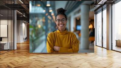 Confident young woman in glasses and a yellow sweater smiling in a modern office environment Wall mural