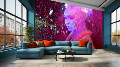 A beautiful young girl is exposed to ultraviolet light. Her face and body are covered with multi colored  powder paint which makes her appear as if she glows. Wall mural