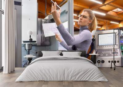 A young woman works as a computerized  numerical control technician. She is seen at her workplace wearing a blue overall.  Wall mural