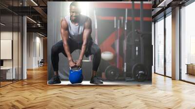 Strong adult black African men swing kettlebell to do crossfit exercise and weight lifting inside of fitness gym to workout for body strength and firm arms muscle and good physical body health. Wall mural