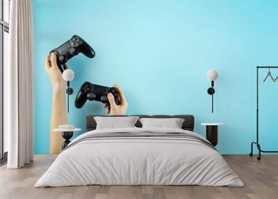 Two black joystick in hands isolated on pastel blue background Wall mural