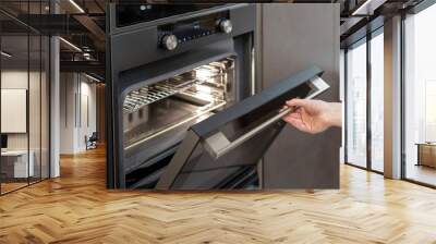 Woman hand opening built-in oven in black kitchen cabinet Wall mural