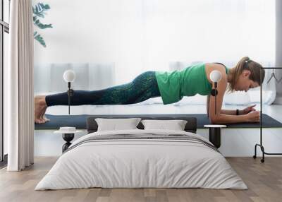 Young sporty woman standing in plank pose on fitness mat Wall mural