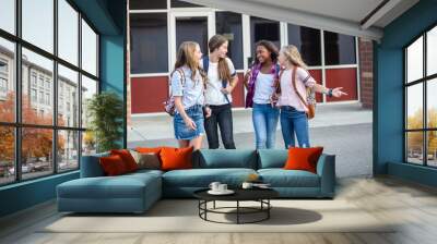 Candid photo of a group of teenage girls socializing, laughing and talking together at school. A multi-ethnic group of real junior high aged students walking outside a school building Wall mural