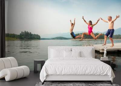 Group of kids jumping off the dock into the lake together during a fun summer vacation. Wall mural