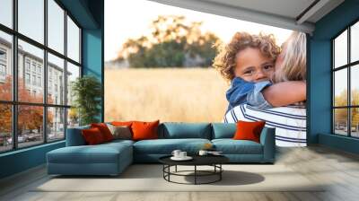 The face of an adorable curly haired African American boy in the arms of his mother in the outdoor sunlight. A happy and content expression as the mom shows love and affection to her son Wall mural