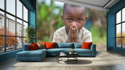 A young child kneeling with hands clasped in prayer, surrounded by nature. Wall mural