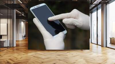 closeup of a young man wearing latex gloves while is using his smartphone Wall mural